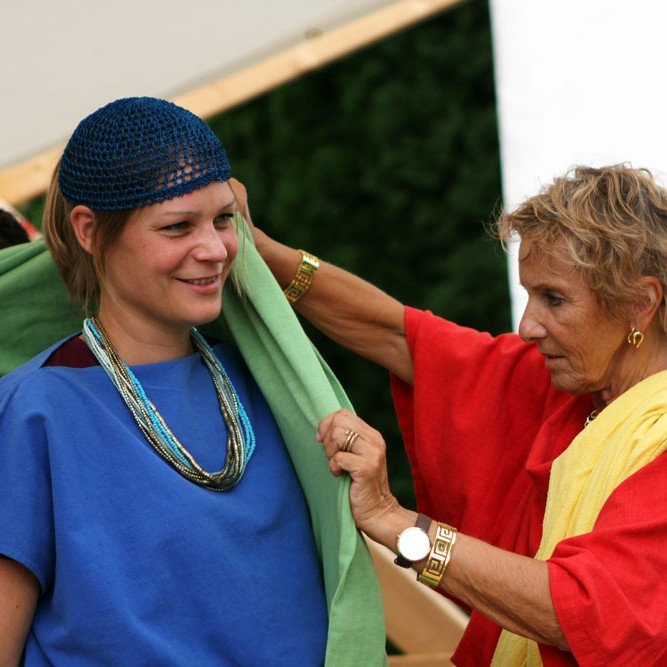 Frau hilft Jugendlicher beim Einkleiden (beide in römischem Gewand)
