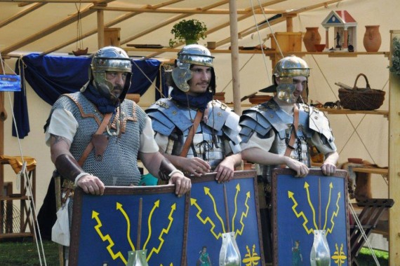 Drei Männer in römischer Legionärs-Ausrüstung mit großen blauen Schildern vor sich