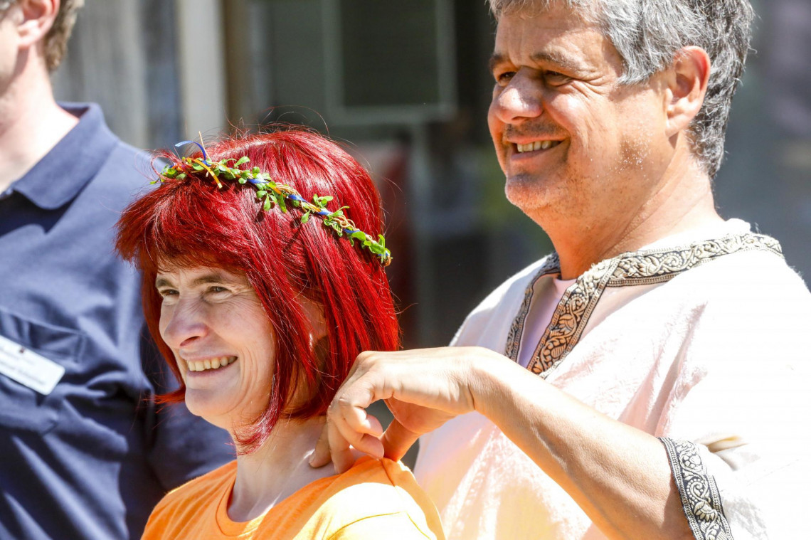 Lachende Frau mit Blumenkranz und lachender Mann in römischer Tunika