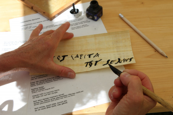 Nahaufnahme Hände; Schreiben mit schwarzer Tinte auf Papyrus an Tisch