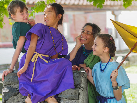 Drei M&auml;dchen und eine Frau in r&ouml;mischer Kleidung stehen im Tempelbezirk des APC vertraut beieinander 