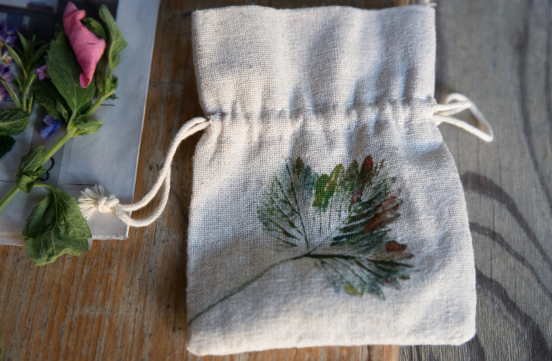 Ein mit Stempeldruck verziertes Kr&auml;uters&auml;ckchen liegt auf einem Holztisch, daneben Blumen Kr&auml;uter